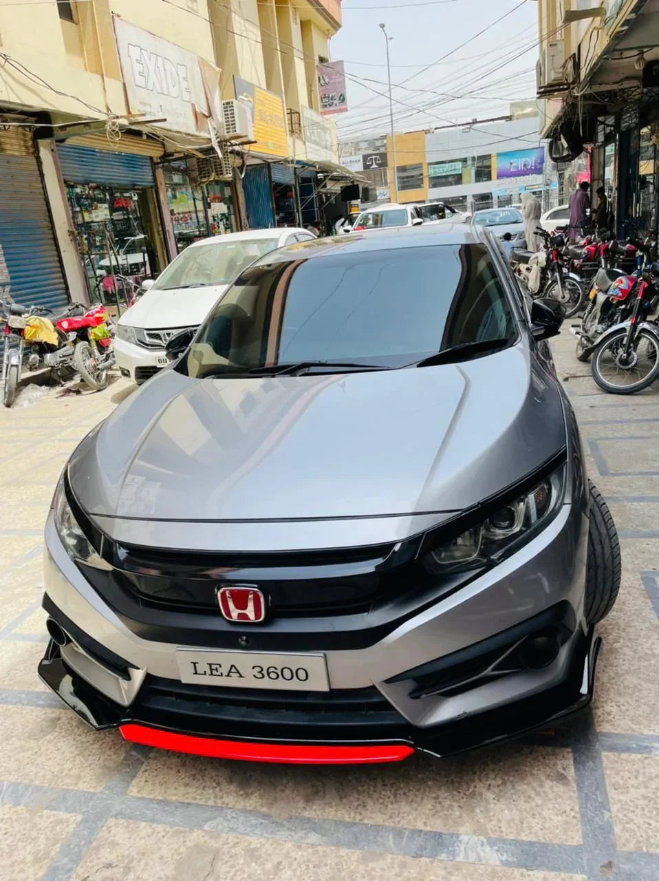 Gray Honda Civic with red front splitter, parked on a busy street in Pakistan