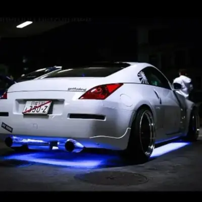 White Nissan 350Z with blue underglow LED lights, custom body kit, and wide rims in garage
